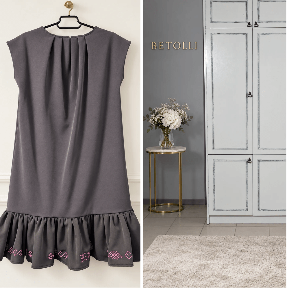 BETOLLI Laimdota grey dress with cap sleeves, neckline pleats and pink Latvian folk embroidery along the ruffle hem, displayed on a hanger.